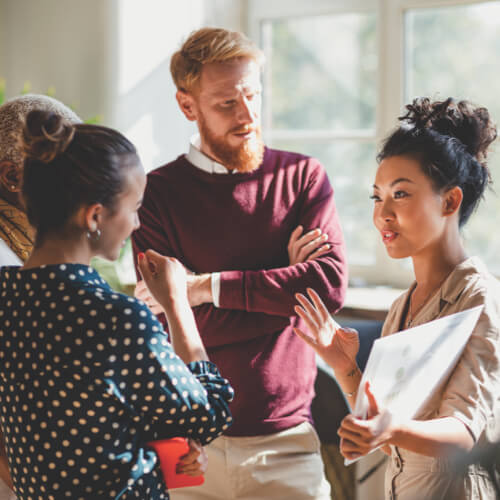 A group of young professionals meeting in a casual setting, female is gesturing with hands while others listen