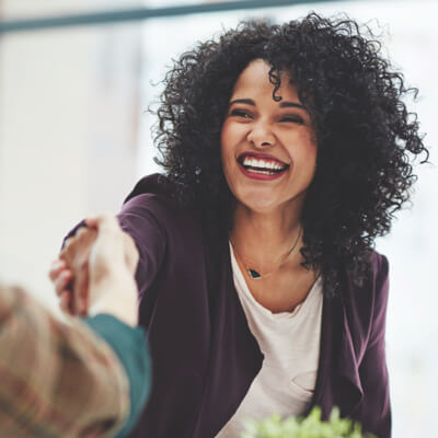 Woman smiling at someone just off camera, reaching out to shake hands