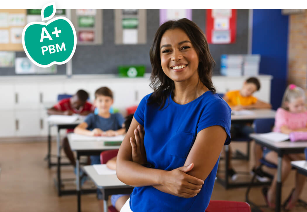 A teacher stands before her classroom, smiling at camera. Class is out of focus in the background. An apple icon overlays the photo with the text "A+ PBM".