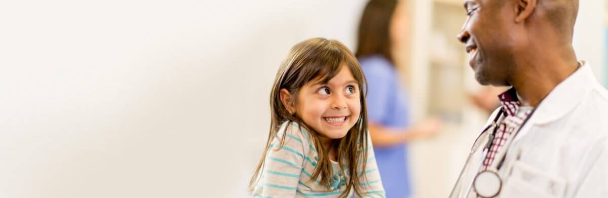 Little girl smiling bashfully at a doctor who is smiling in return.