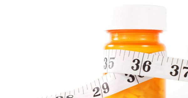 A medication bottle wrapped with a tape measure against a white background.