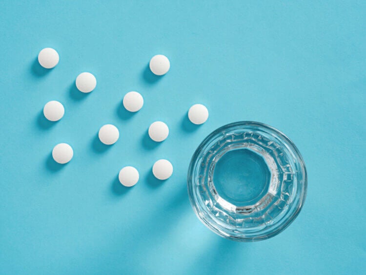 Looking down at white pills and a glass of water on a blue surface