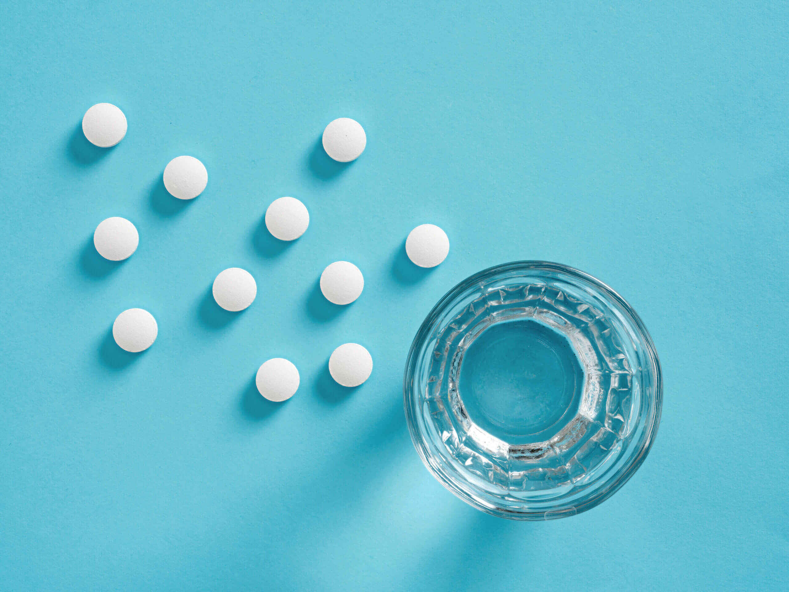 Looking down at white pills and a glass of water on a blue surface
