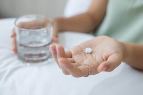 Adult woman holding a white pill and glass of water.