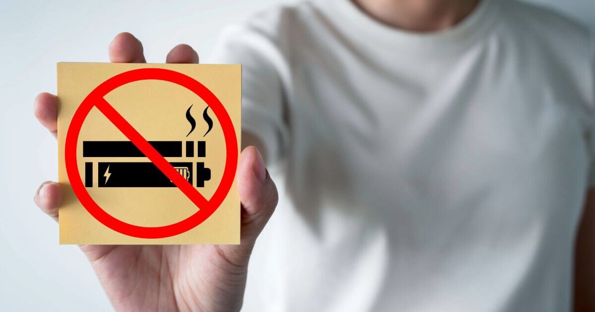 person with white shirt holding sign that has cancel sign with vape